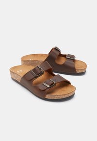 Smeđe kožne sandale s dvostrukim podesivim kopčama, plutenom unutrašnjosti i teksturiranom gumenom potplatu. Dizajn s otvorenim prstima, ležeran stil.