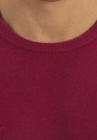 Pull en tricot bordeaux avec un col ras du cou côtelé. Texture douce et couture régulière. Vue en gros plan mettant en valeur la couleur et le matériau.