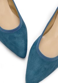 Pantofole blu in suede con un design a punta. Bordo rifinito con tessuto blu testurizzato. Fodera interna liscia di colore tan a contrasto.