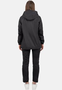 Giacca nera impermeabile con cappuccio, polsini elasticizzati e orlo regolabile, abbinata a jeans scuri e sneaker bianche.