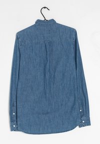 Camisa de denim de manga larga en azul claro. Presenta un collar, puños con botones y un yugo trasero con un solo pliegue. Textura suave y diseño casual.