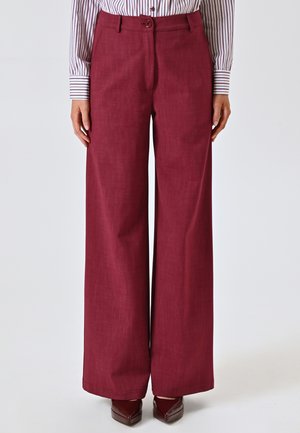 Pantalons larges en tissu bordeaux riche, avec une texture lisse, une fermeture à bouton unique et une coupe ajustée.