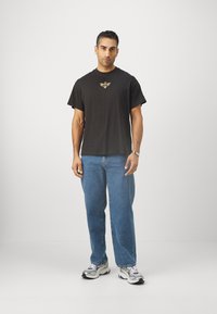 Sort kortærmet t-shirt med et gul grafikdetalje, parret med lyseblå lige jeans og grå sneakers med accenter.