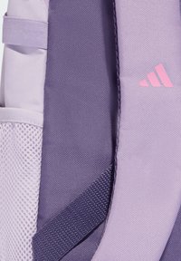 Fioletowy plecak z teksturowanej tkaniny, siateczkową boczną kieszenią i różowym logo. Prezentuje różnorodne odcienie fioletu oraz gładkie, trwałe materiały.