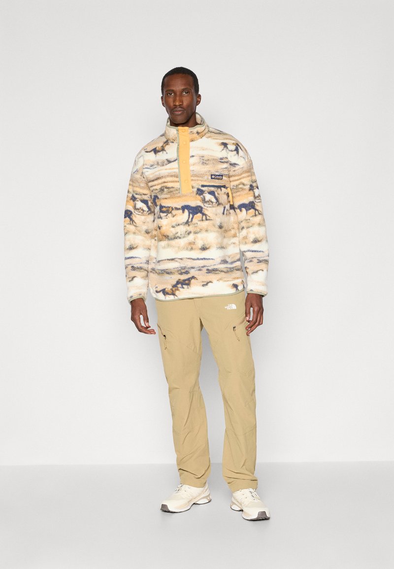 Pullover in fleece con base beige, stampa animalier blu e colletto con zip. Abbinato a pantaloni beige e sneakers bianche.