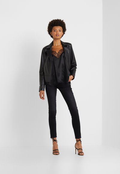 Black leather jacket over a black satin top with sheer detailing, paired with dark skinny jeans and strappy high heels.