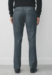 Grau gestreifte Hose mit taillierter Passform, ausgestattet mit Gesä�ßtaschen und einer glatten Textur, kombiniert mit schwarzen Schuhen.