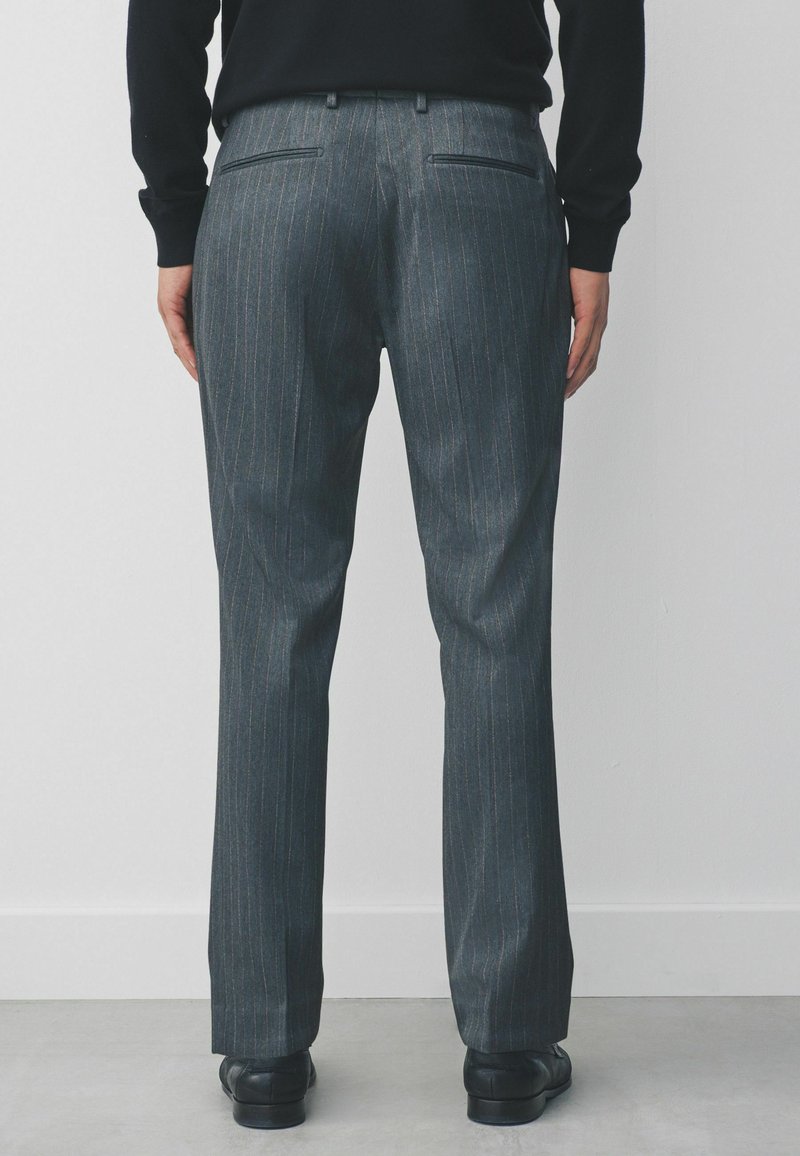 Grau gestreifte Hose mit taillierter Passform, ausgestattet mit Gesäßtaschen und einer glatten Textur, kombiniert mit schwarzen Schuhen.