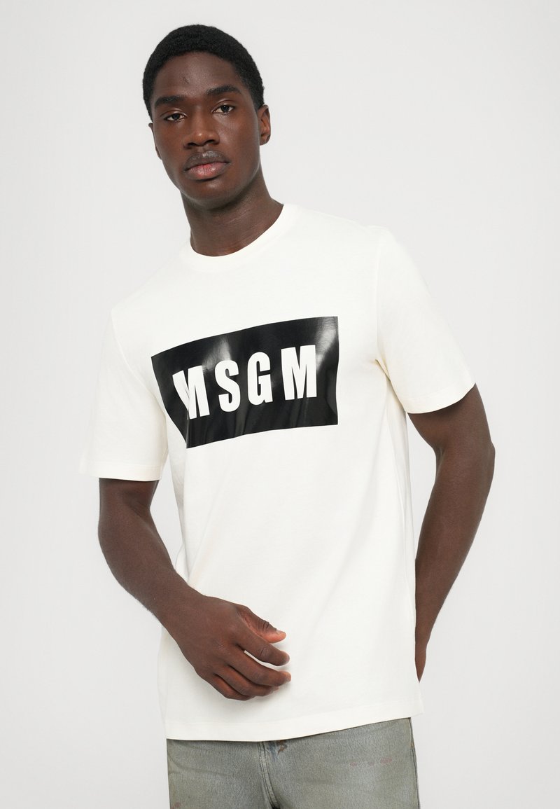 White graphic t-shirt featuring a black rectangular logo with “MSGM” in bold white letters. Short sleeves, crew neckline, casual fit.