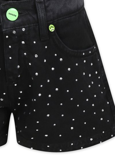 Shorts in denim nero decorati con borchie argentate, dotati di un bottone verde con una faccina sorridente e un design classico delle tasche.