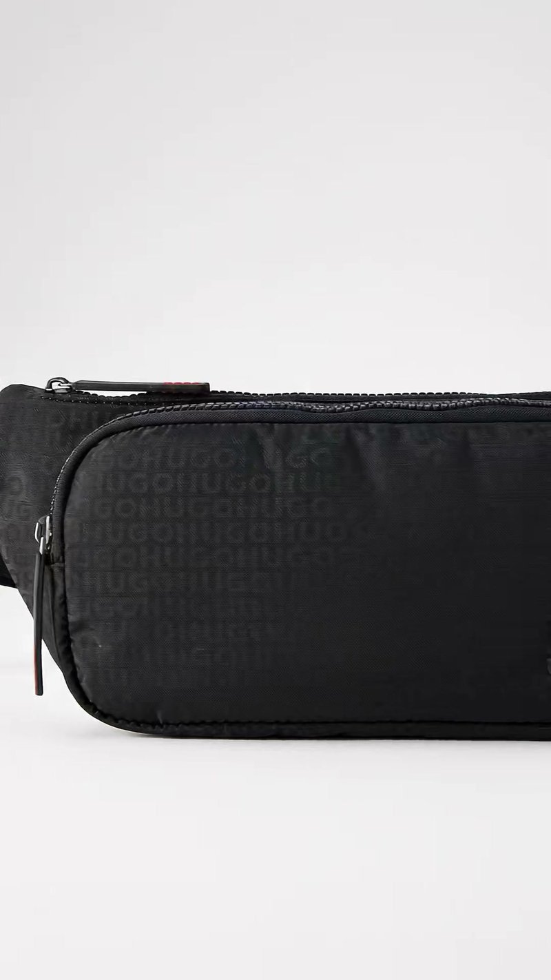 Sac banane en tissu noir avec deux compartiments zippés et un motif de texte embossé discret sur la poche avant.