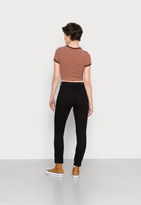 Jeans skinny pretos com uma cintura alta, combinados com uma t-shirt cropped com riscas em tom ferrugem. O modelo usa ténis de cano alto em tom beige.