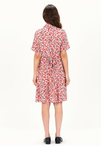 Rode bloemenjurk met korte mouwen, detail met strik aan de achterkant en een wijde rok. Heeft blauwe en witte bloemenpatronen op een lichte achtergrond.