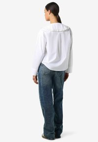 Biała koszula z długim rękawem z koronkowym wykończeniem na kołnierzyku, zestawiona z luźnymi, wyblakłymi niebieskimi dżinsami. Tkanina wydaje się gładka, o swobodnym kroju.