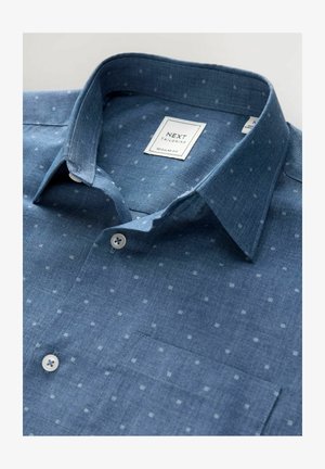 Modrá chambray košeľa s klasickým strihom, s golierom na gombíky, malým bielym bodkovaným vzorom a náprsním vreckom. Viditeľná nálepka značky Next.