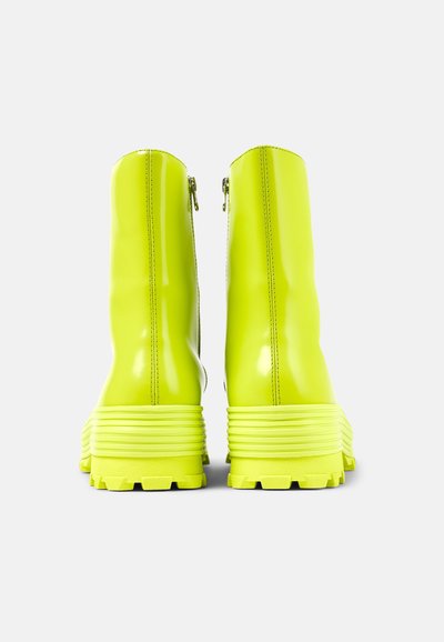 Neon yellow glossy ankle boots with a textured sole and vertical zipper closure at the back. Chunky design with ribbed accents.
