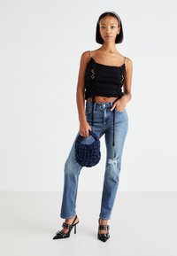 Black crocheted crop top with adjustable ties, paired with light blue distressed jeans and black high-heeled mules. Holding a navy textured bag.