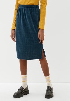 Person iført en blå ribbet midi-nederdel med sideslids, gul langærmet top, stribede sokker og sorte chunky loafers.