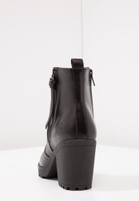 Bottines en cuir noir avec un bout arrondi, un talon bloc haut et une fermeture éclair. Elles présentent des surpiqûres décoratives et une languette de tirage.