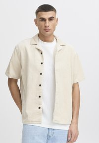 Cream corduroy shirt jacket with a relaxed fit, short sleeves, black buttons, and a flat collar, layered over a white t-shirt.