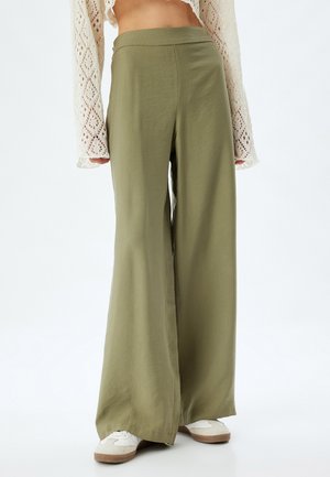 Pantalones de pierna ancha en verde oliva, hechos de una tela suave. Presentan una cintura alta y una textura ligera. Combinados con zapatillas blancas.