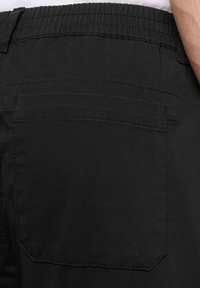 Pantaloni neri con una texture liscia, vita elasticizzata e una singola tasca sul retro con dettagli a doppio punto.