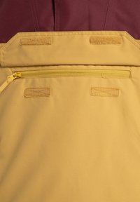 Gelbes Außenmaterial mit einer glatten Textur verfügt über eine Reißverschlusstasche und drei Klettverschluss-Patches. Der obere Abschnitt ist tief burgunderrot.