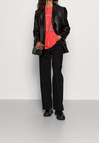Blazer de piel negra sobre una camiseta con estampado de pañuelo rojo, combinado con pantalones acampanados negros y unos zapatos negros gruesos. Incluye un bolso cruzado sencillo.