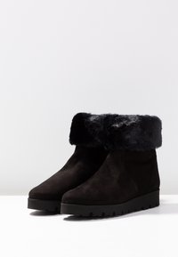 Botas de tobillo negras de ante con un borde de piel sintética. Punta redondeada y suela de goma con un leve patrón de tracción. Diseño simple y elegante.