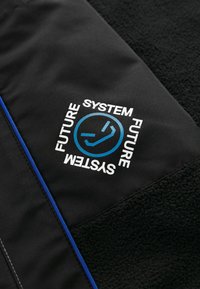 Czarna kurtka z teksturowanym panelem z polaru, niebieskimi akcentami oraz białym graficznym logo z napisem "SYSTEM FUTURE" w kwadratowym wzorze.