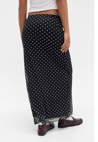 Melna polka punktu maksi svārki, kas izgatavoti no viegla materiāla, ar caurspīdīgu apakšmalu un sānu šķēlumiem. Saskaņoti ar tumšiem apaviem.