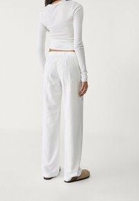 Biały obcisły top z długim rękawem i luźne białe spodnie. Top ma prążkowaną fakturę; spodnie są gładkie, z elastyczną talią i bocznymi kieszeniami.