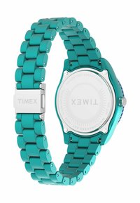 Zegarek Timex z turkusowym metalowym paskiem i kopertą. Posiada okrąłą tarczę z przezroczystym cyferblatem i srebrnymi detalami.