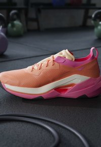 Chaussure de sport légère corail et rose avec semelle rembourrée sur le sol de la salle de sport, kettlebells et corde d’entraînement en arrière-plan flou.
