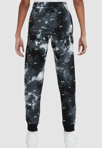 Svart och grå joggingsbyxor med ett tie-dye-mönster, prydda med spridda vita Nike-loggor, elastisk midja och ribbad nederkant.
