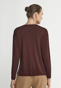 Mörk röd långärmad tröja med rund hals, ribbade mudd och nederkant. Materialet verkar mjukt med en slät yta och har en avslappnad passform.