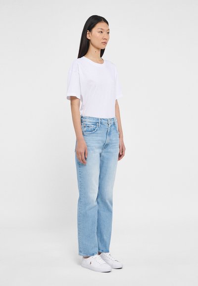 Jeans din denim de culoare albastră deschisă cu croi drept, asortați cu un tricou din bumbac alb, de croi lejer, și teniși albi. Fundal cu suprafață plată.