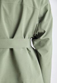 Indumento verde oliva con cintura, realizzato in un tessuto liscio e leggermente testurizzato. Presenta dettagli arricciati e un design semplice sul retro.