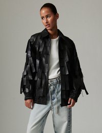 Μαύρο δερμάτινο μπουφάν bomber με υφασμένη φράντζα, κλείσιμο με φερμουάρ και ριμπ μανσέτες. Φορεμένο πάνω από άσπρο τοπ και τζιν σε ανοιχτή απόχρωση.