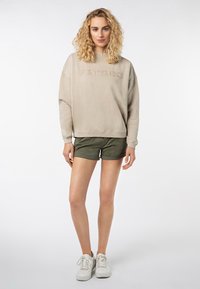 Beige sweatshirt met "FUN TIMES" geborduurd, gecombineerd met olijfgroene shorts. Model draagt witte sneakers en toont een casual outfit.