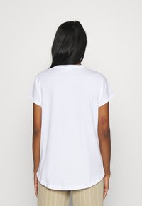 Camiseta de algodón blanca con mangas cortas, escote redondeado y un dobladillo ligeramente curvado. La tela parece suave y lisa.