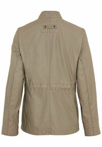 Khaki jakke med ståkrave, lange ærmer og rygstykke. Har to synlige stiklinger og et mærke på kraven.