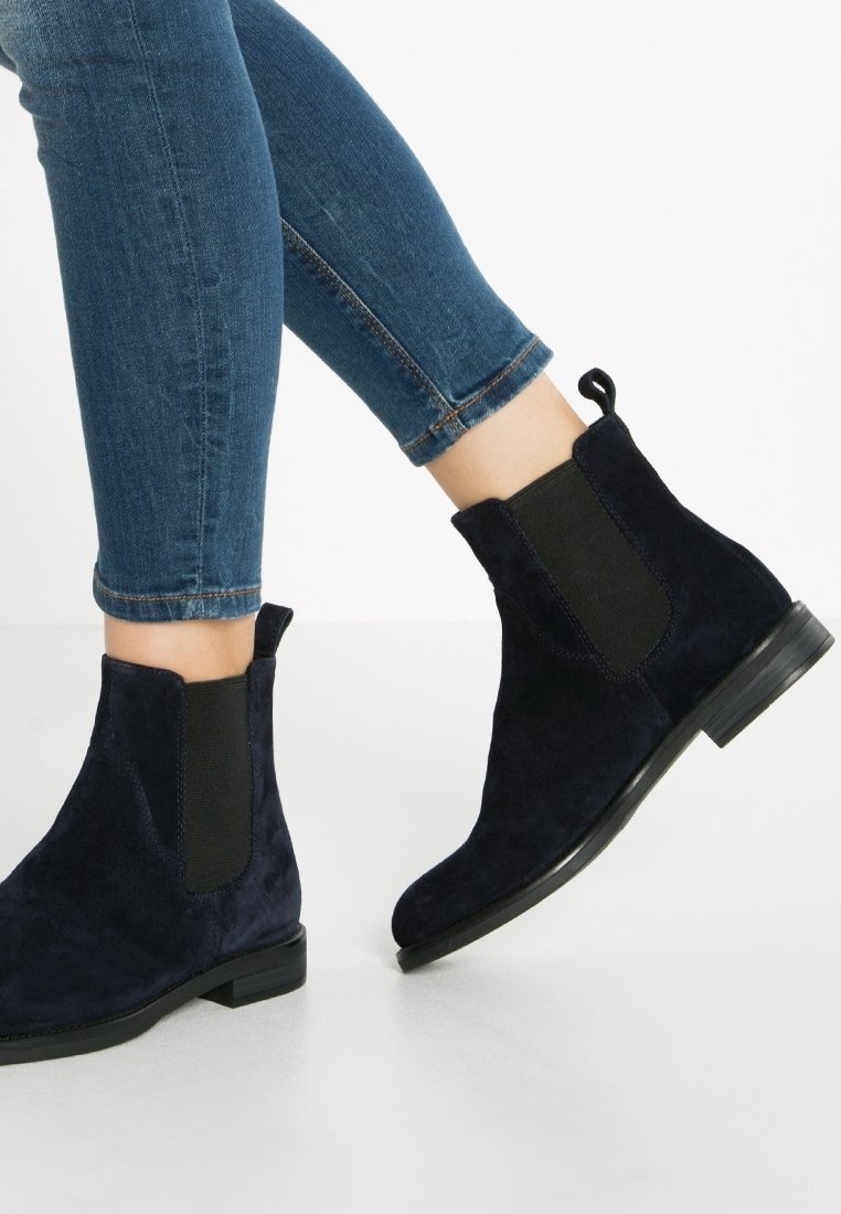 Botines de ante azul marino con paneles elásticos en los laterales, suelas planas y tiradores. Combinados con unos vaqueros cortos de color azul oscuro.