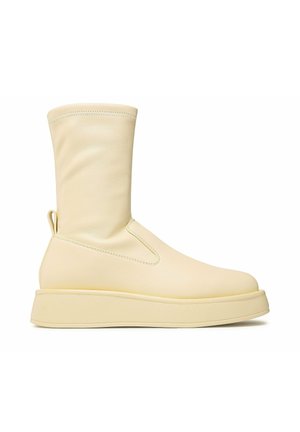 Kremowy, sięgający do połowy łydki but z gładkiej skóry, zaokrąglonym noskiem, pętelką u pięty oraz grubą, płaską podeszwą.