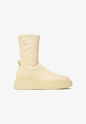 Kremowy, sięgający do połowy łydki but z gładkiej skóry, zaokrąglonym noskiem, pętelką u pięty oraz grubą, płaską podeszwą.