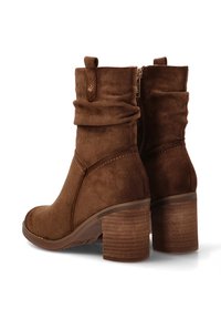 Botas de tobillo de ante marrón con un diseño arrugado, un cierre de cremallera lateral y un tacón de madera grueso y texturizado. Punta redondeada y detalles de costura.