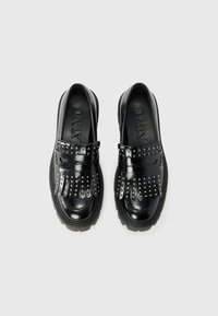 Black loafers with a shiny finish, featuring studded accents and fringe details. Thick rubber soles provide traction.