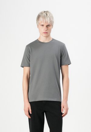 Camiseta gris de manga corta hecha de tela suave con un diseño clásico de cuello redondo. Combinada con pantalones negros rectos.