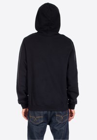 Felpa nera con cappuccio e una texture morbida, caratterizzata da un design semplice e una tasca a marsupio. Indossata con jeans in denim blu.