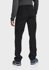 Schwarze Outdoor-Hosen mit einem dehnbaren Bund, tailliertem Schnitt und minimaler Naht. Kombiniert mit grauen Wanderschuhen mit grünen Akzenten.